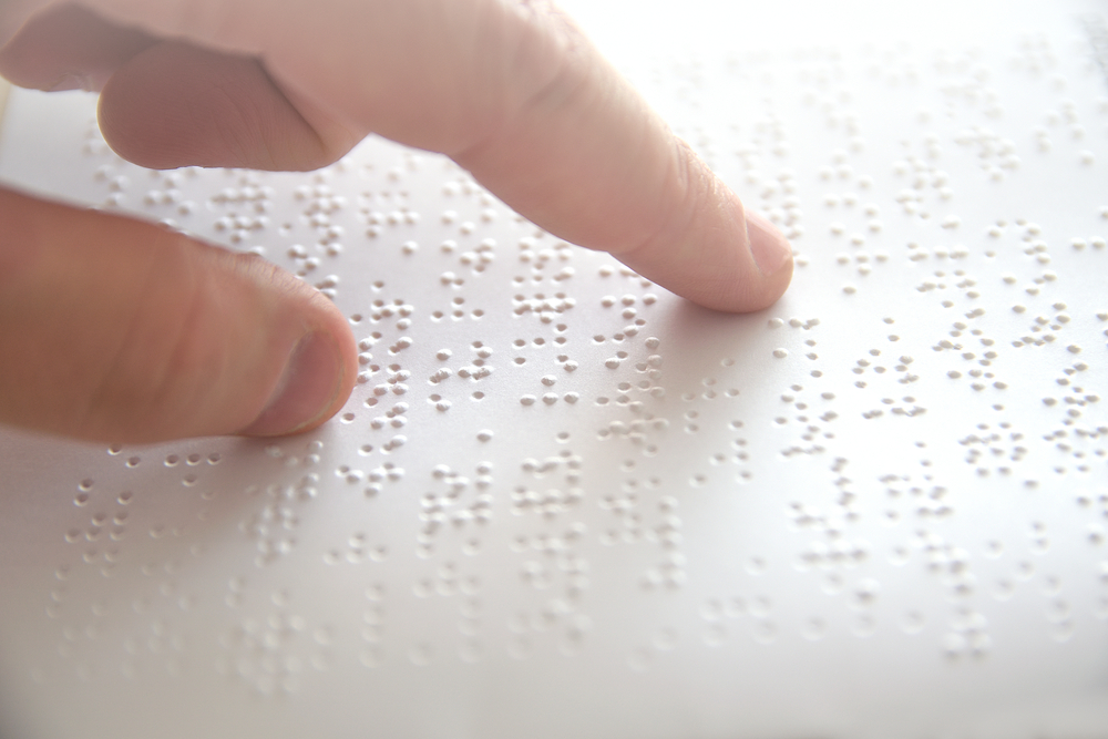 Close-up of a person’s finger reading raised Braille text on a white page.